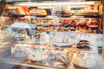 Assortment of desserts on cafe showcase. Variety of cakes tiramisu pies with different flavours fruits in store.