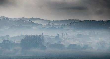 Fog over the city on a slope in cloudy weather, cypresses stick out, Corfu, Greece