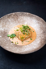 Gourmet fried skrei cod fish in Thai curry with chili and sprouts as closeup on a modern design plate with copy space