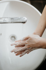 Closeup of a woman washing her hands in bathroom to prevent Covid-19 viral infection. Recommended washing with soap and running water during coronavirus pandemic. Top shot view.