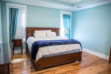 Large blue master bedroom with a king-sized bed, furniture and drapes curtains on the windows with hardwood floors
