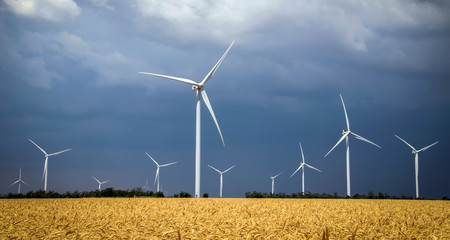 Wind turbines and agricultural field on a summer cloudy day. Energy production, clean and renewable energy.