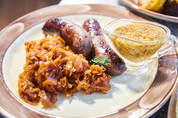 The grilled sausages with sauerkraut and mustard sauce lies on a plate, Tableware, Fork, knife, napkins
