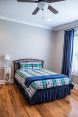 Light gray teenage boy bedroom with a wood bed and plaid bedspread and curtains in shades of blue, green and white