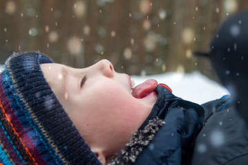 The European boy sticks out his tongue and catches snowflakes with his tongue. Close-up portrait....