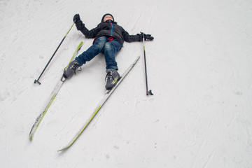 The boy is tired and lies resting in the winter on the snow. A European child with skis and ski poles.