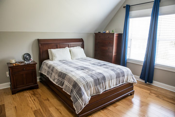 Light gray teenage boy bedroom with a wood bed and plaid bedspread and curtains and other furniture