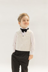 Portrait of a caucasian boy 3-5 years old in a classic men 's white shirt, black tie butterfly and vest made of dressing fabric. Child smiles and poses on White background, copyspace