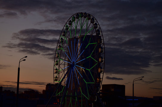 silhouette of a Ferris wheel against the sunset sky with clouds