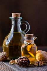 Obraz na płótnie Canvas Concept of vegetable fat and oils for cooking and cosmetology. Glass bottle with bright yellow essence, raw walnut peeled and in their shells. Wooden board, dark wooden background, close up, macro