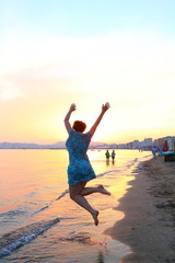 silhouette of happy woman standing and jumping in the water of the ocean while watching the sunset