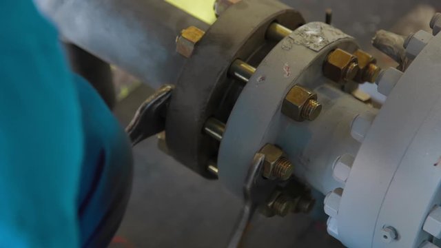 Worker tightens the bolt with a wrench. Worker assembles Oil and Gas equipment in industrial plant. The group metering stations allow taking measurements of raw oil mass flow and free oil gas volume.