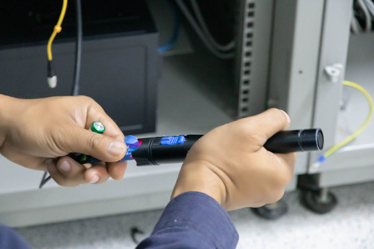 Closeup hand holding fiber optic cables with visual fault locator laser in the networking room.Visual Fault Locator is a cable continuity tester that locates fiber