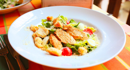 Caesar salad with croutons, quail eggs, cherry tomatoes and grilled chicken in a white plate on a table in a restaurant. Flatlay. Top down. 