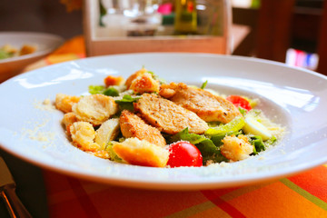 Caesar salad with croutons, quail eggs, cherry tomatoes and grilled chicken in a white plate on a table in a restaurant