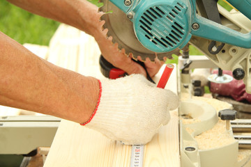 A male carpenter machine operator with a pencil in his hand measures the cutting board with a tape measure on a woodworking machine