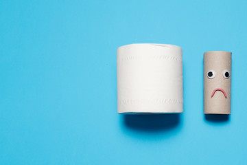 Full toilet paper roll next to a sad and frowning empty toilet paper roll with googly eyes and mouth on a blue background with copy space and room for text with a right side composition.