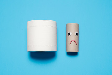 Full toilet paper roll next to a sad and frowning empty toilet paper roll with googly eyes and mouth on a blue background with copy space and room for text