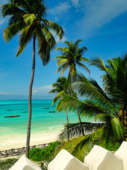 Fototapeta na wymiar Traumkulisse Raffaello Werbung, Kokospalmen und Fernweh am weißen Strand mit türkisem Meer auf Sansibar, Fischerboote und Horizont im Hintergrund