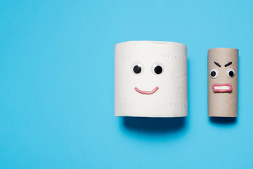 Happy smiling full toilet paper roll next to an angry empty toilet paper roll with googly eyes and mouth on a blue background with copy space and room for text with a right side composition.