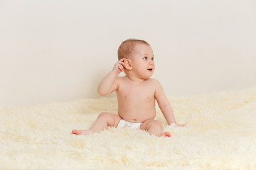 cute baby girl in a diaper sits well on a fluffy blanket on a white background