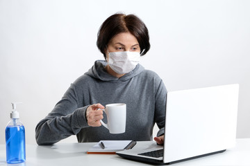 masked woman works on the computer and drinks coffee at the table