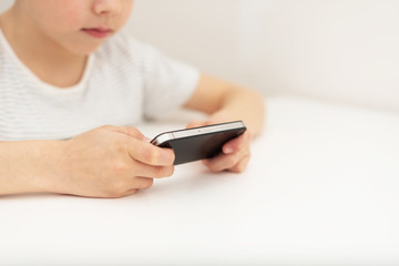 A boy sits at a table and plays on the phone