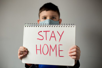 A male child holding a stay home sign wearing a handmade cloth  face mask, the concept of flatten the curve stay home during pandemic of coronavirus