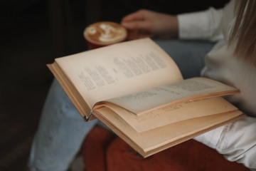 Fototapeta premium Woman with cup of coffee reading book indoors, closeup