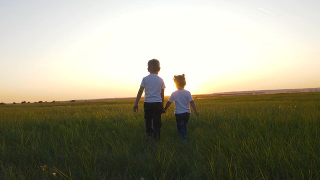 Children boy and girl walking on the green grass holding hands.