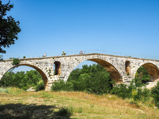Fototapeta na wymiar Bicyclists on an old stone bridge in the French countryside with blue sky and copy space.