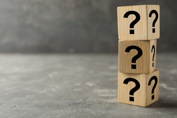 Wooden cubes with question marks on grey stone table. Space for text