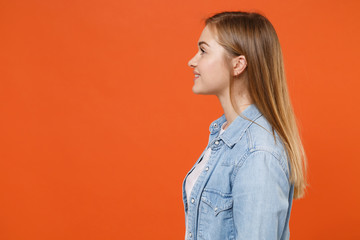 Side view of beautiful young woman girl in casual denim clothes posing isolated on orange wall background studio portrait. People sincere emotions lifestyle concept. Mock up copy space. Looking aside.
