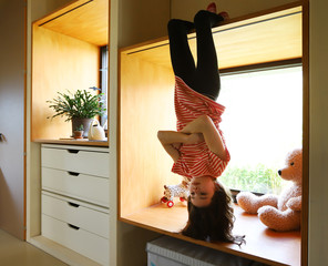 Ein Mädchen hängt während der Coronakrise gelangweilt kopfüber am Fenster am 01.04.2020.