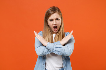 Irritated young woman girl in casual denim clothes posing isolated on orange wall background. People lifestyle concept. Mock up copy space. Showing stop gesture with crossed hands screaming swearing.