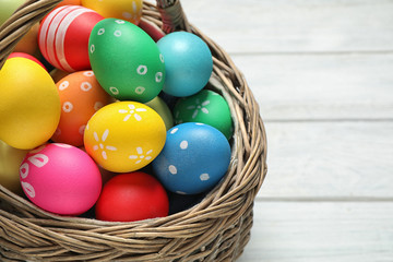 Colorful Easter eggs in basket on white wooden table, closeup