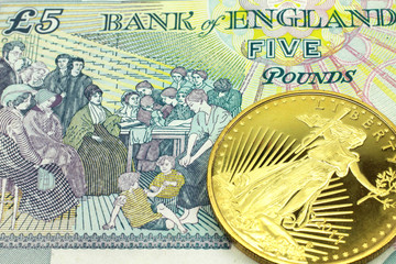 A macro image of a colorful five pound note from the UK with a gold coin.  Shot close up.