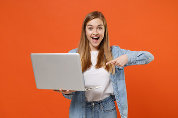 Excited young woman girl in casual denim clothes posing isolated on orange wall background studio portrait. People lifestyle concept. Mock up copy space. Pointing index finger on laptop pc computer.