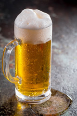 Light frothing beer in a glass, on an old background.