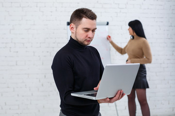 Manager businessman male announcer stands with a laptop while a woman writes a business promotion...