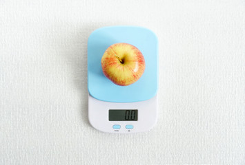 Red glossy apple on scales, on white background. Template calorie count for diet and sports. Closeup photo