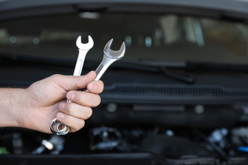 Professional auto mechanic holding wrenches near modern car in service center, closeup of hand