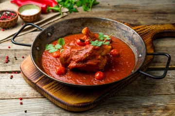Leg of lamb in tomato sauce on old wooden table