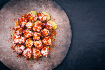 Traditioneller gegrillter spanischer Oktopus pulpo a la gallega mit Bratkartoffel und Chili als Draufsicht auf einem Modern Design Teller mit Textfreiraum rechts © HLPhoto