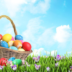 Wicker basket with Easter eggs in green grass against blue sky. Space for text