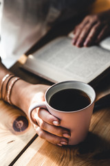Woman in the morning drinks coffee and reads old book in a white shirt. Education, drink. manicure