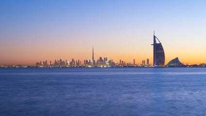 Burj Al Arab in Jumeirah Island or boat building with waves on sea beach, Dubai Downtown skyline, United Arab Emirates or UAE. Financial district in urban city. Skyscrapers at sunset. © tampatra