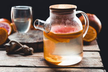 Citrus tea in a transparent teapot and a glass, healthy drink on a wooden background.