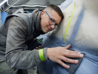 cheerful, young man with glasses polishes, primes and paints a car in the garage