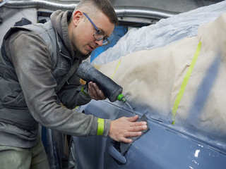 cheerful, young man with glasses polishes, primes and paints a car in the garage